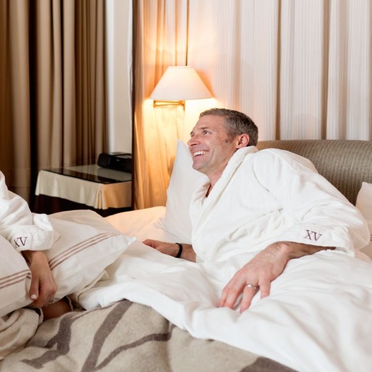A couple both in our fifteen beacon robes laying in bed cozening up with our Frette linens.