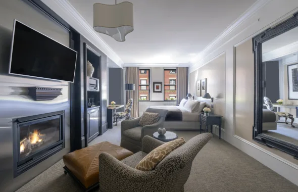 Studio at XV Beacon with lounge chairs, ottoman, large mirror, bed, workstation, end table, TV and fireplace.