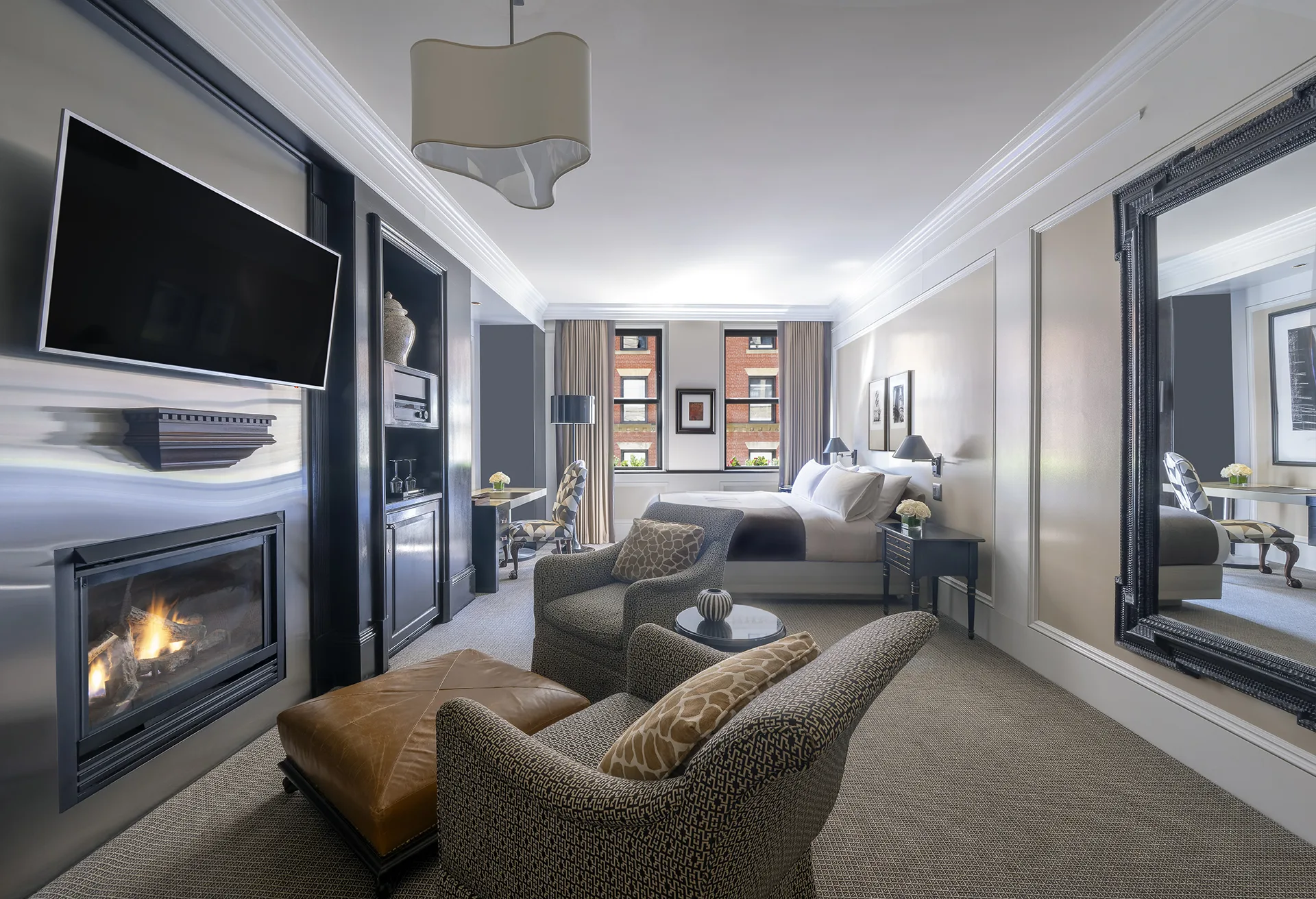 Studio at XV Beacon with lounge chairs, ottoman, large mirror, bed, workstation, end table, TV and fireplace.