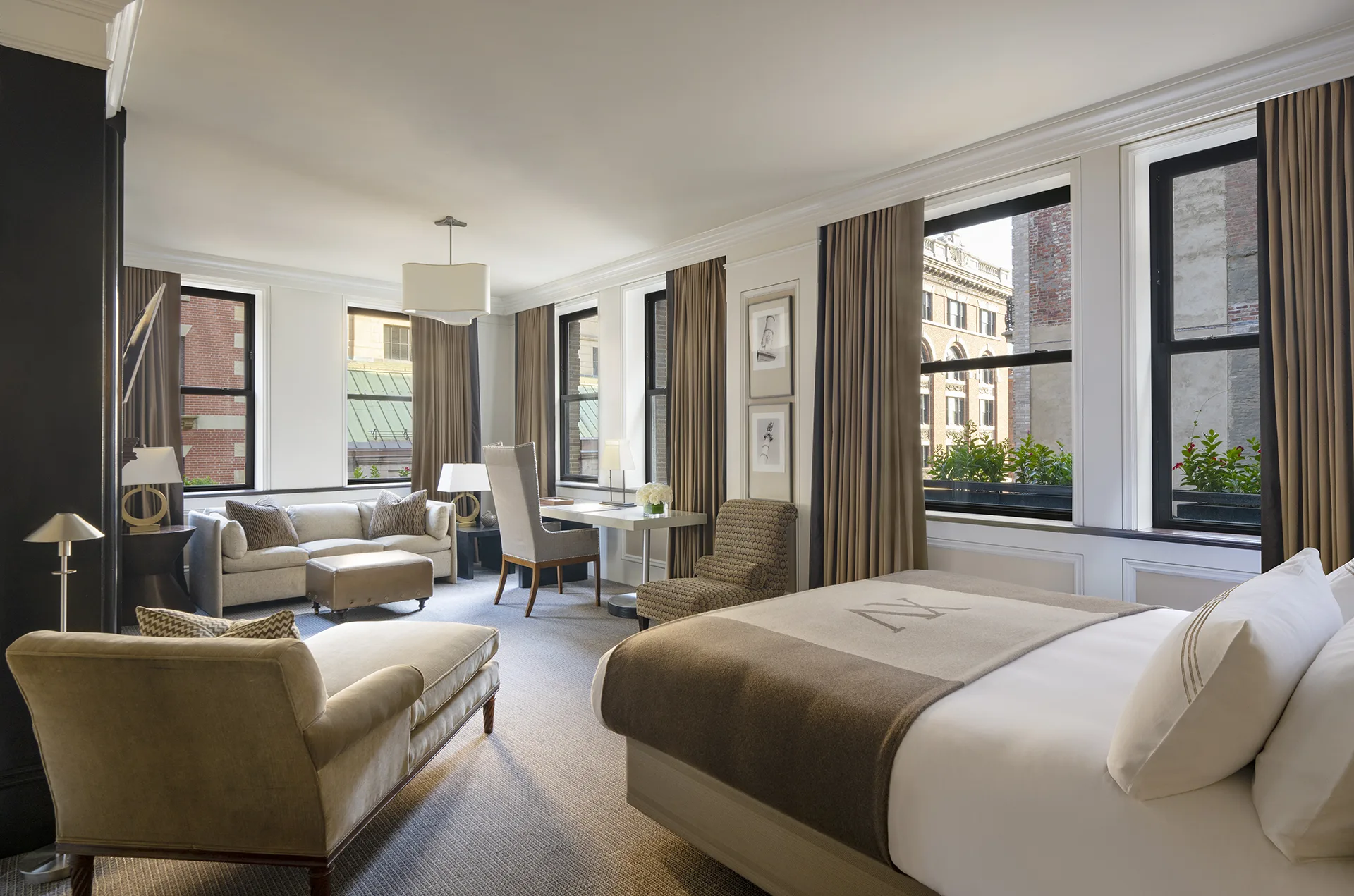 Studio room at XV Beacon with chaise lounge, ottoman, sofa, bed, workstation, large windows, TV and fireplace.