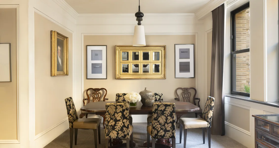 Dining room with plant-patterned chairs, oak dining table, wall art, large windows and a floral centerpiece.