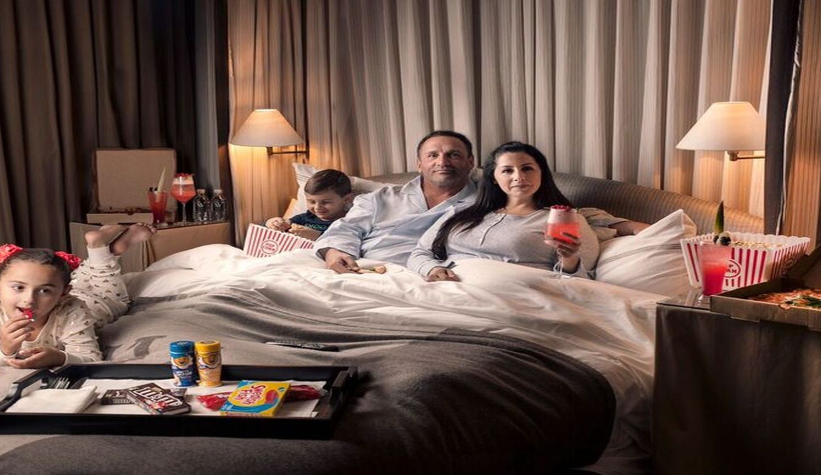 Family of four in bed enjoying our movie night themed in-room dining packages.