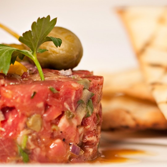 steak tartar with a green pickle and a green olive on top. Serviced with toasted pita bread