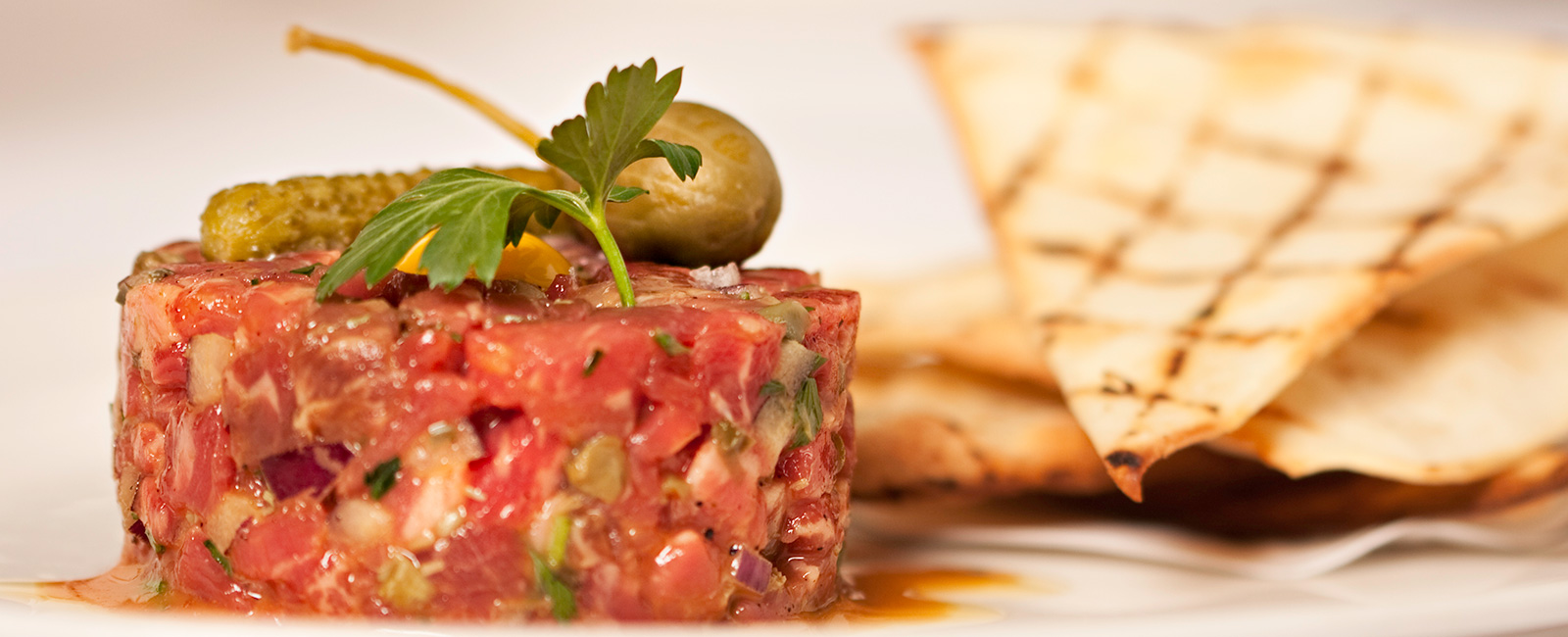 steak tartar with a green pickle and a green olive on top. Serviced with toasted pita bread