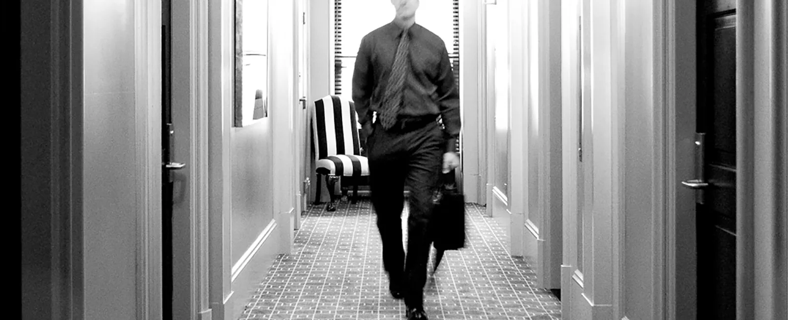 black and white photograph of a guest walking towards the elevators from his room.