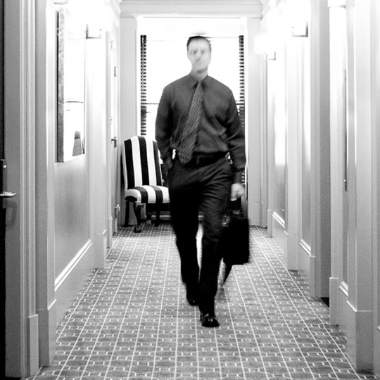 black and white photograph of a guest walking towards the elevators from his room.