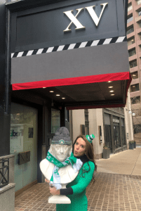 Photo of our hotel's general manager, Amy Finsilver dressed up for St. Patty's Day while holding the Ben Franklin Statue