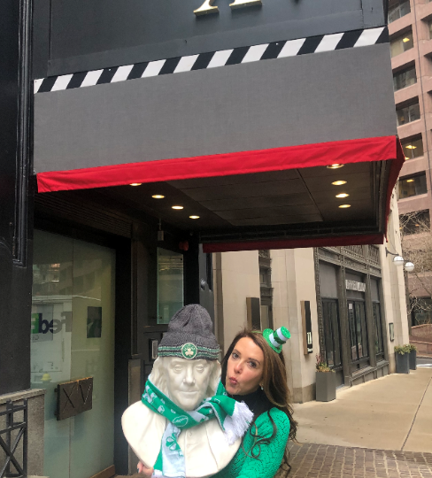 Photo of our hotel's general manager, Amy Finsilver dressed up for St. Patty's Day while holding the Ben Franklin Statue