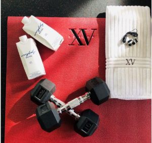 Photo of our XV Beacon Yoga mat, 10 pound free weights, XV Beacon hand towel with headphones on top of the towel along side our new water from everybody water