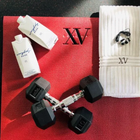Photo of our XV Beacon Yoga mat, 10 pound free weights, XV Beacon hand towel with headphones on top of the towel along side our new water from everybody water
