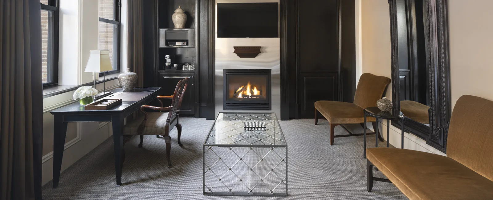 Elegant sitting room with a workstation, two plush bench-style chairs, a fireplace and a glass coffee table.