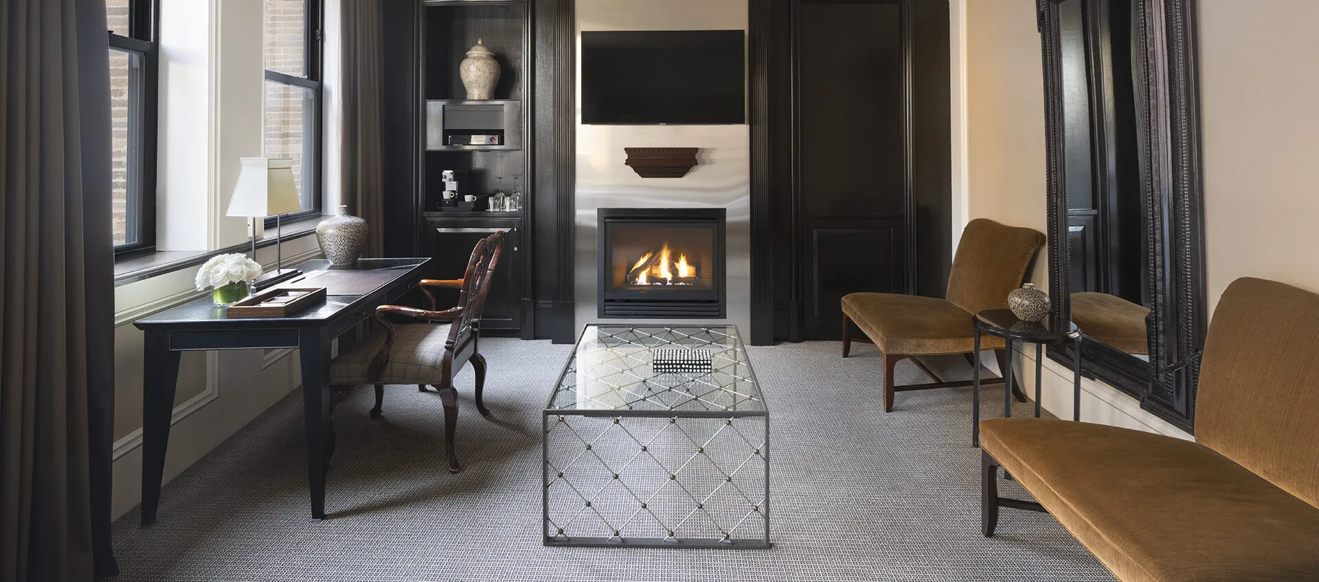Elegant sitting room with a workstation, two plush bench-style chairs, a fireplace and a glass coffee table.