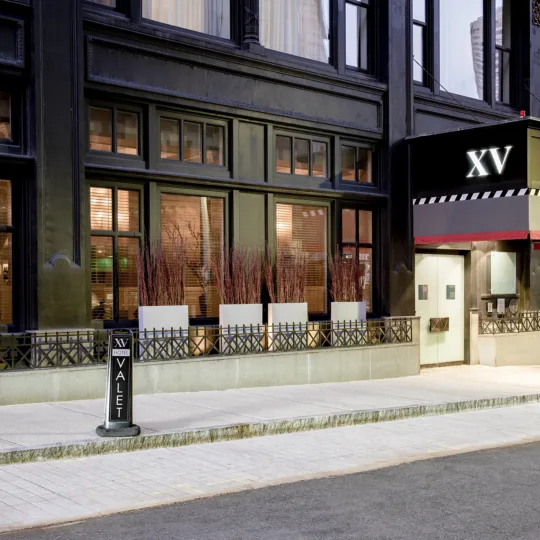 Exterior of the hotel's facade with entry doors, large windows, foliage, wrought-iron railing and a valet parking sign.