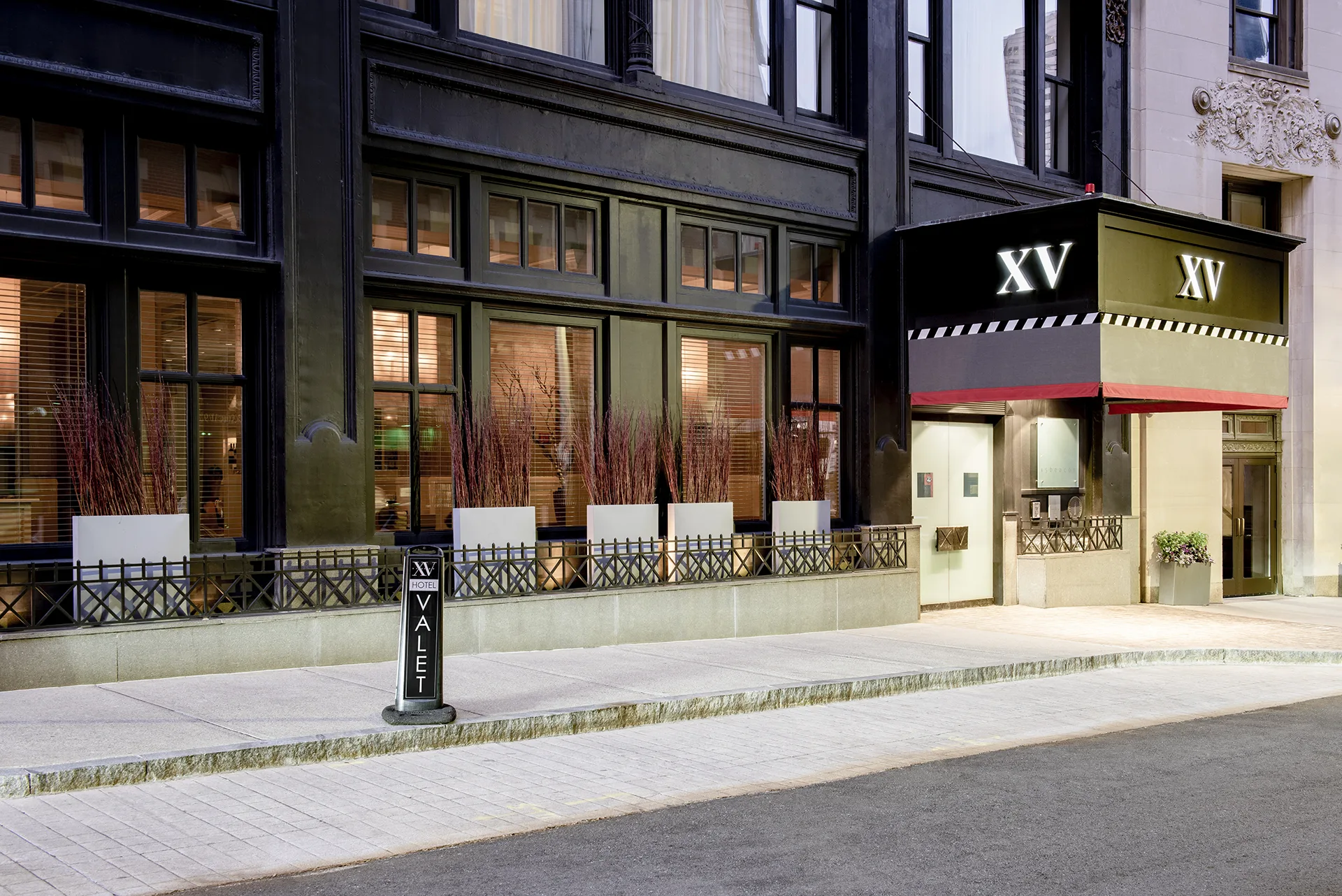 Exterior of the hotel's facade with entry doors, large windows, foliage, wrought-iron railing and a valet parking sign.