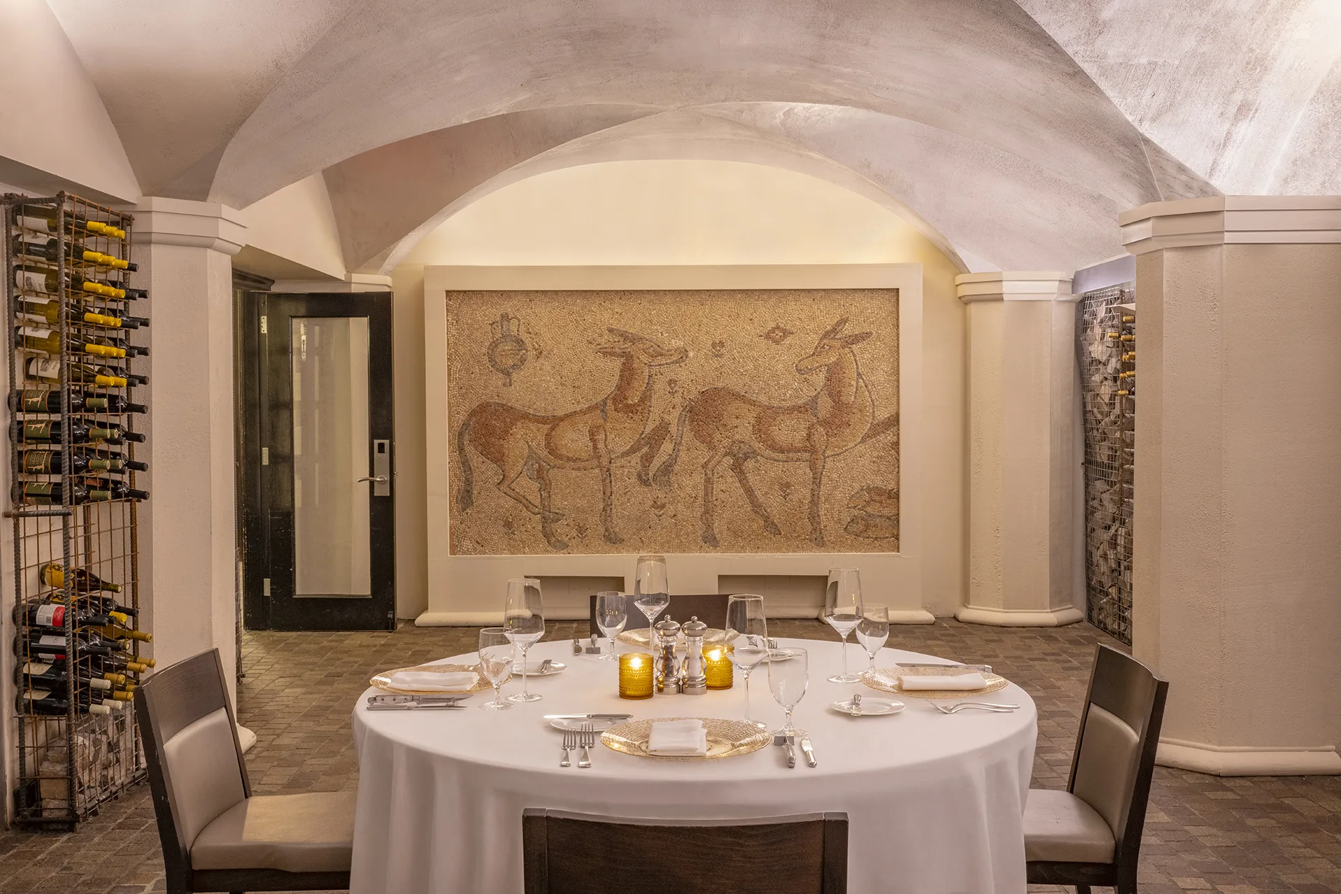 Dining area with vaulted ceilings, wildlife wall mosaic, elegant table settings, two chairs and a fully stocked wine rack.